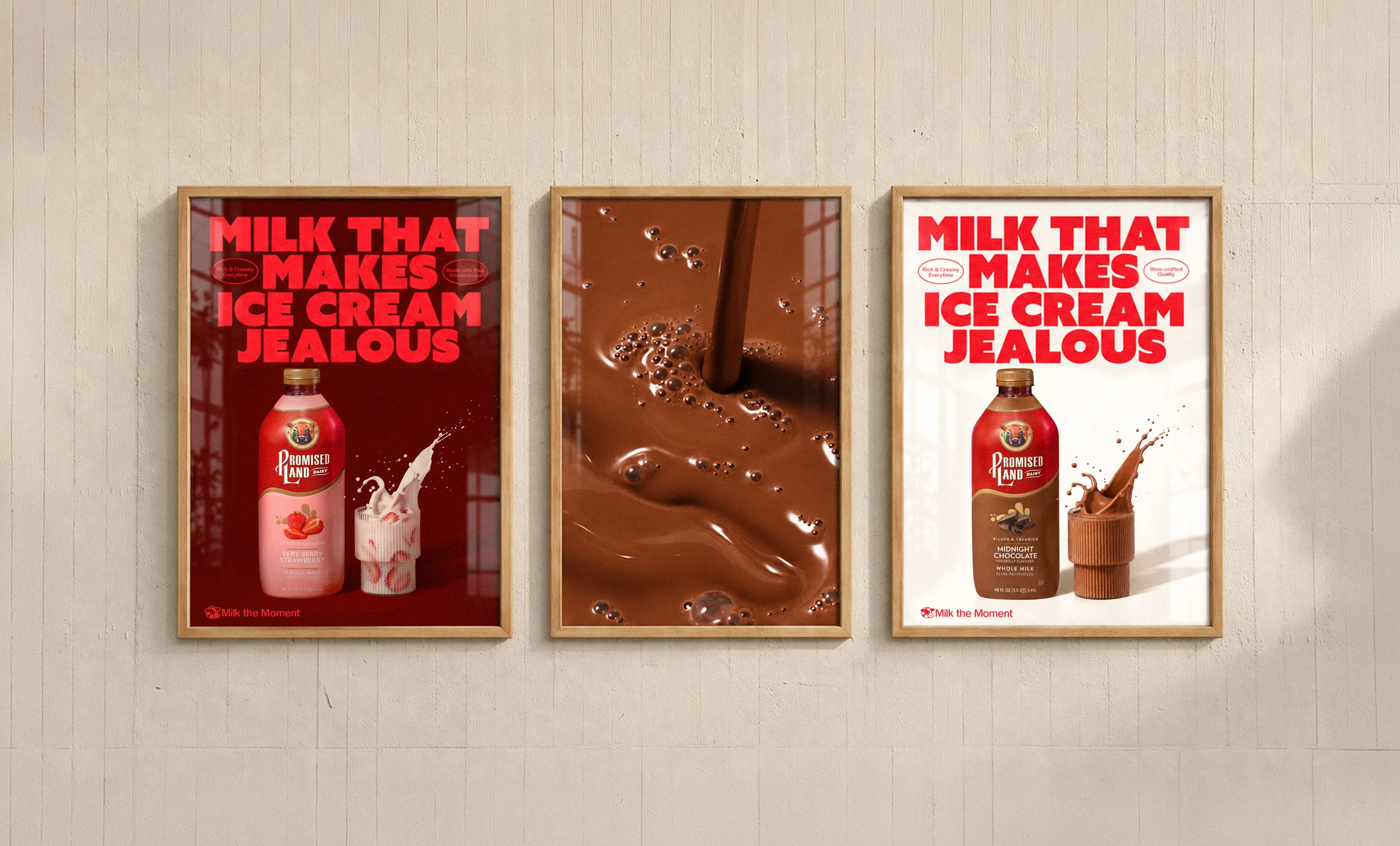 Three framed posters on a pale wooden wall: two read “Milk that makes ice cream jealous”, stamped “Rich & Creamy Everytime” and “Slow-crafted Quality”, one with a Promised Land Dairy Very Berry Strawberry bottle and one with a Midnight Chocolate bottle, both signed “Milk the Moment”; the middle poster is a macro of pouring chocolate milk